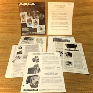 May include: A collection of black and white brochures advertising Arca-Swiss cameras and accessories. The brochures feature images of the cameras and text describing their features. The text includes the phrase "The cameras for creative professionals".