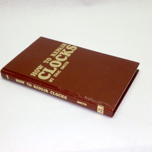 May include: A brown hardcover book titled "HOW TO REPAIR CLOCKS" by Eric Smith. The title and author's name are in gold lettering. The book's spine also features the title and the author's last name.