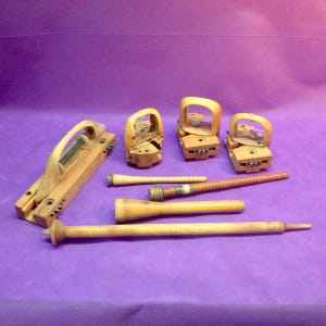 May include: A set of vintage wooden knitting tools, including three wooden bobbins, two wooden spindles, and a wooden knitting loom. The tools are all in good condition and have a natural wood finish.