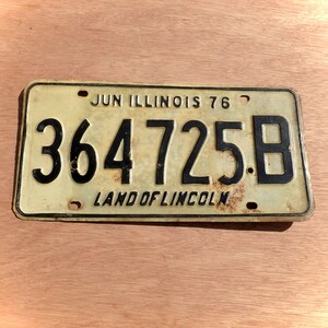 May include: A vintage Illinois license plate from June 1976. The plate is yellow with black lettering and the number 364 725.B. The bottom of the plate reads "Land of Lincoln".