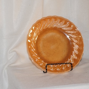 May include: A peach-colored glass plate with a swirl design around the edge. The plate is on a white surface.