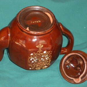May include: A brown ceramic teapot with a gold floral design and a lid. The teapot is marked "JAPAN" on the bottom.
