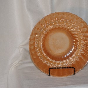 May include: A vintage peach-colored glass plate with a swirling, textured design. The plate is on a white surface.