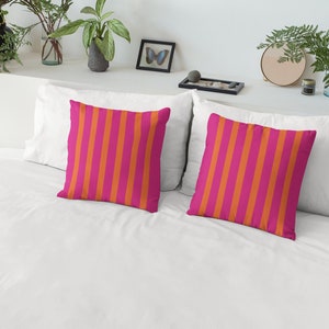 May include: Two decorative throw pillows with a pink and orange striped pattern. The pillows are on a white bed with a white headboard.