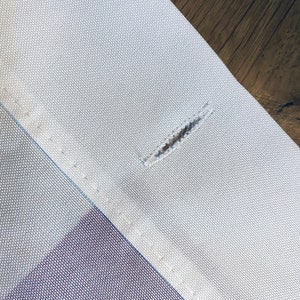 May include: Close-up of a white fabric with a small hole in the centre. The fabric has a subtle texture and is sewn with a straight stitch.