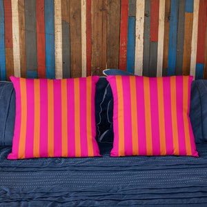 May include: Two pink and orange striped throw pillows on a blue bed with a wooden headboard.