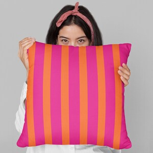 May include: A pink and orange striped throw pillow being held in front of a person's face.