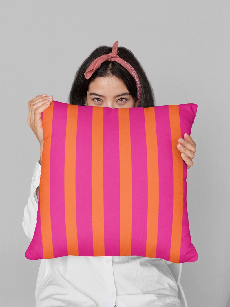 May include: A pink and orange striped throw pillow being held in front of a person's face.