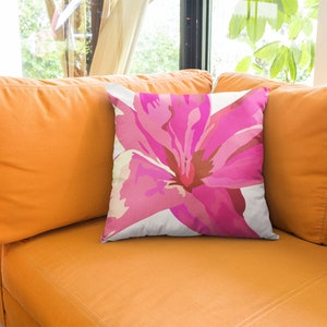Op de afbeelding: Een wit kussen met een roze bloemenpatroon. Het kussen ligt op een oranje bank.
