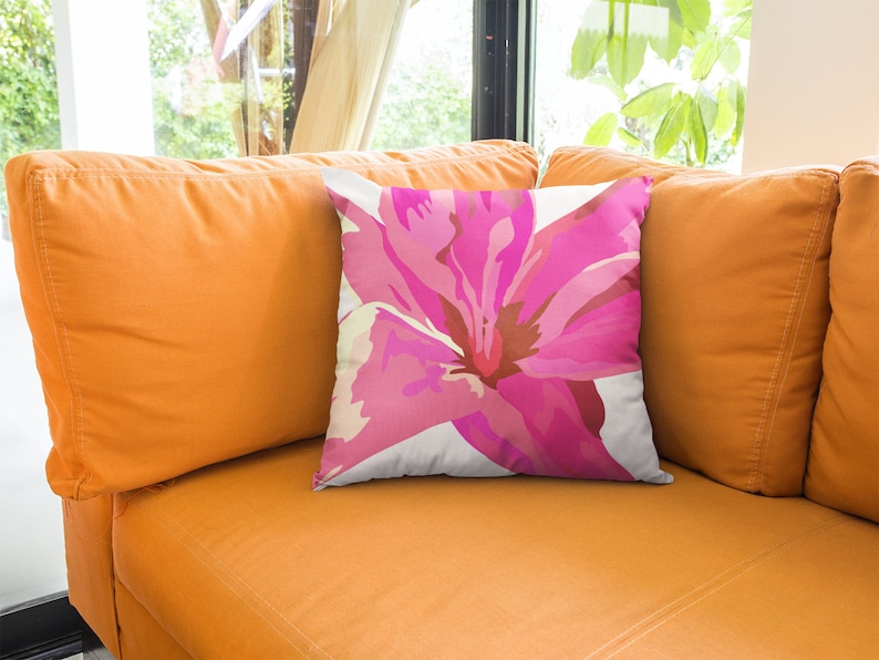 Op de afbeelding: Een wit kussen met een roze bloemenpatroon. Het kussen ligt op een oranje bank.