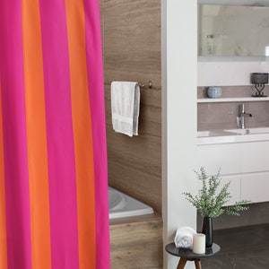 May include: A pink and orange striped shower curtain hangs in a bathroom with a white bathtub and a wooden floor. A white towel hangs on a towel rack on the wall.