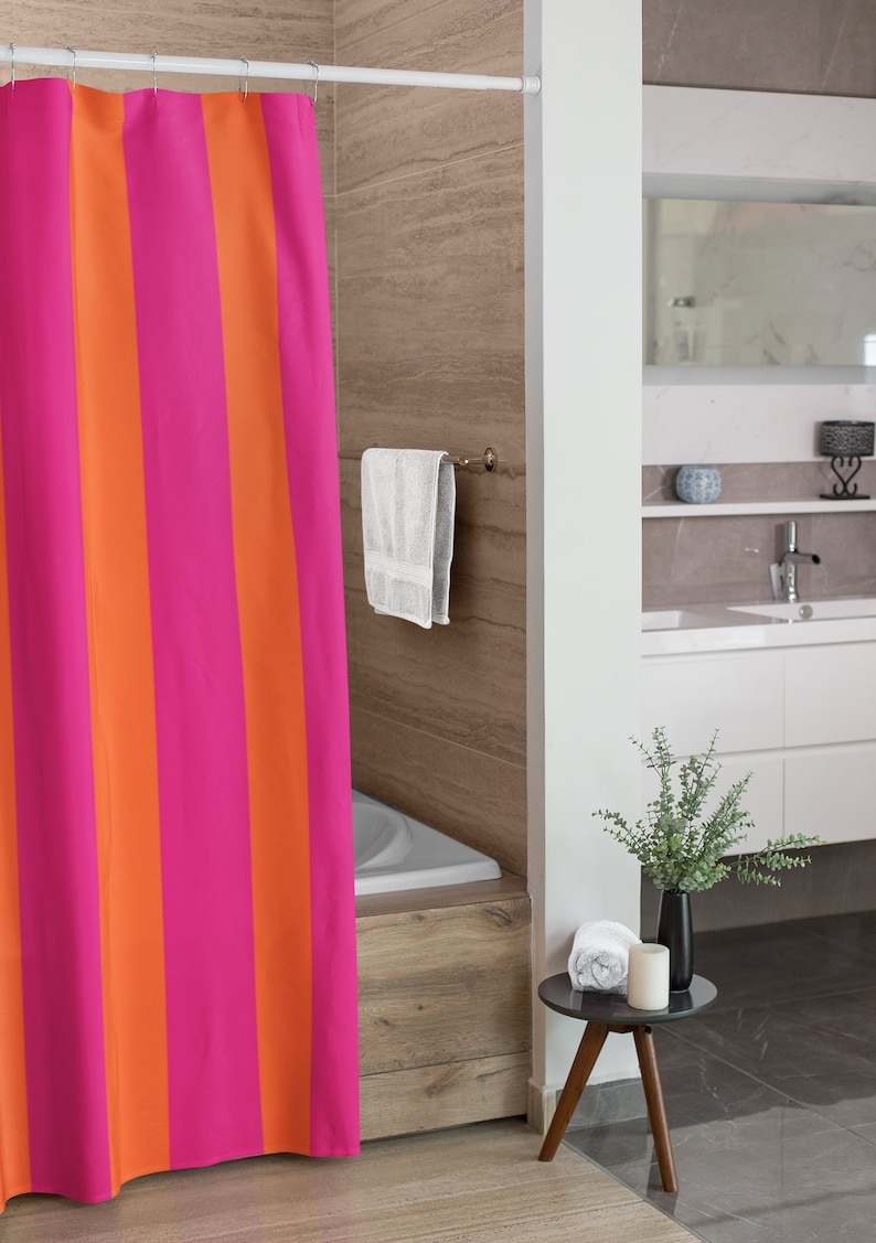 May include: A pink and orange striped shower curtain hangs in a bathroom with a white bathtub and a wooden floor. A white towel hangs on a towel rack on the wall.