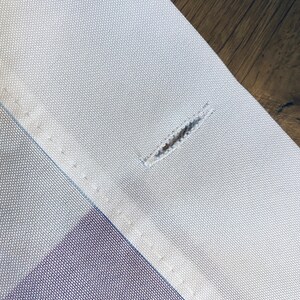 May include: Close-up of a white fabric with a small hole in the center. The fabric has a subtle texture and is sewn with a straight stitch.