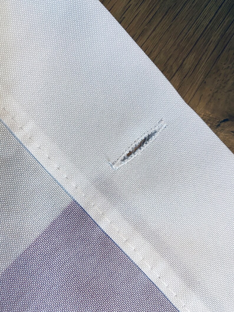 May include: Close-up of a white fabric with a small hole in the center. The fabric has a subtle texture and is sewn with a straight stitch.