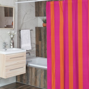 May include: Pink and orange striped shower curtain in a bathroom setting. The curtain is hanging from a white shower rod.