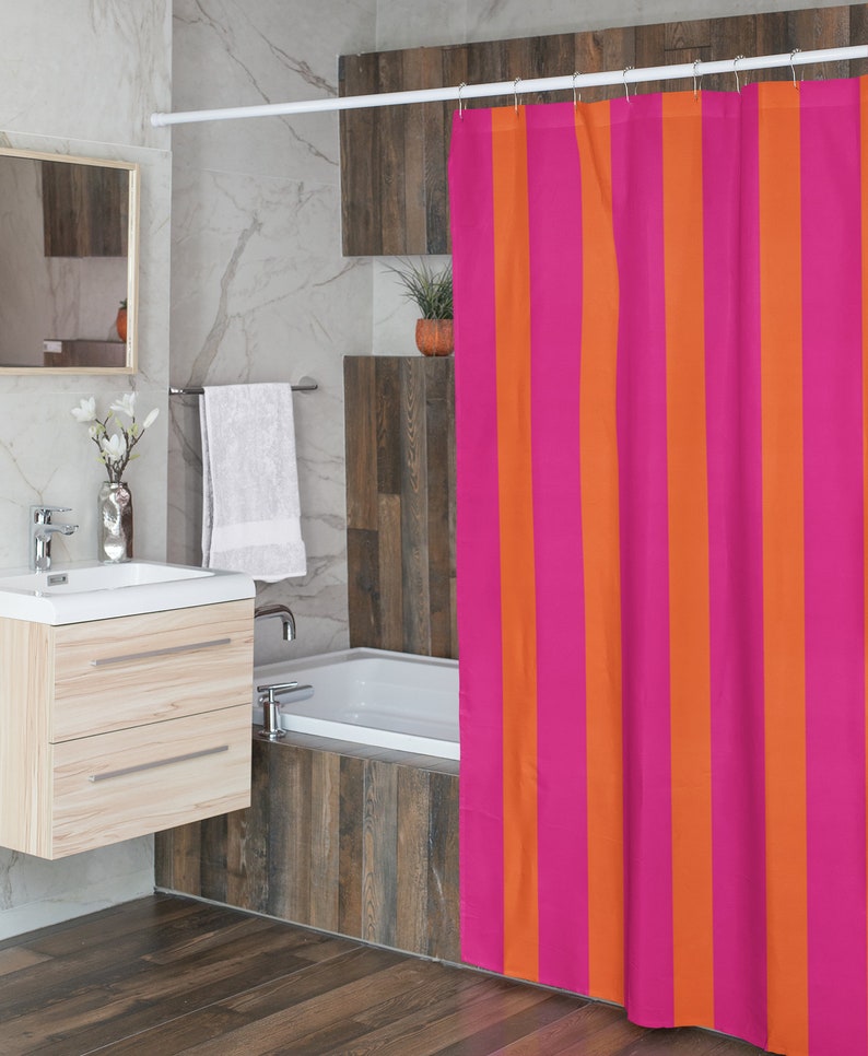 May include: Pink and orange striped shower curtain in a bathroom setting. The curtain is hanging from a white shower rod.