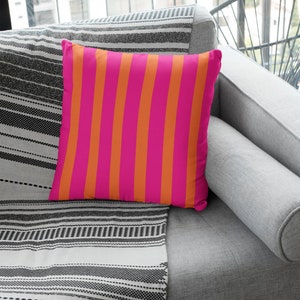 May include: A pink and orange striped throw pillow on a grey sofa with a black and white striped throw blanket.