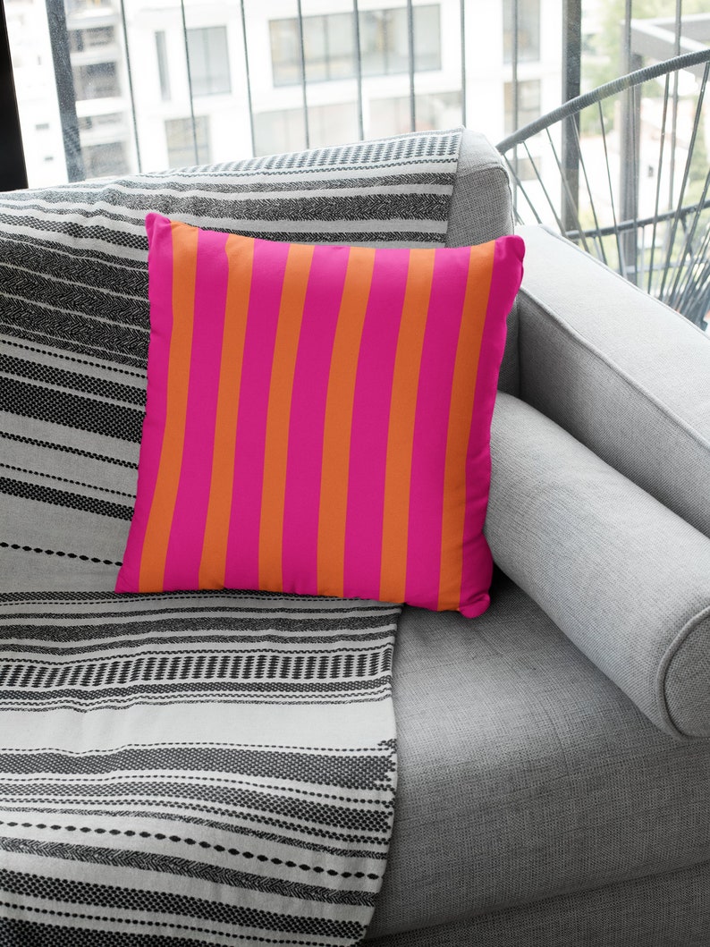 May include: A pink and orange striped throw pillow on a grey sofa with a black and white striped throw blanket.