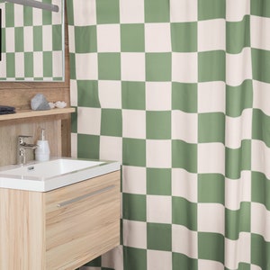 May include: A green and white checkered shower curtain hangs in a bathroom. The curtain is made of a soft, fabric material. The shower curtain is hung on a white shower rod.