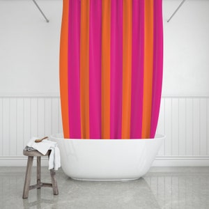 May include: A white bathtub with a pink and orange striped shower curtain in a white bathroom.