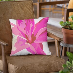 Op de afbeelding: Een bruine leren fauteuil met een roze bloemenkussen. Het kussen heeft een grote roze bloem met witte en rode accenten.