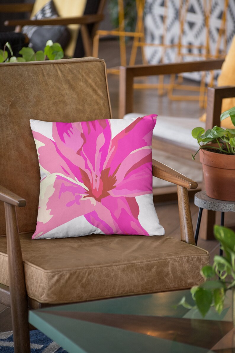 Op de afbeelding: Een bruine leren fauteuil met een roze bloemenkussen. Het kussen heeft een grote roze bloem met witte en rode accenten.