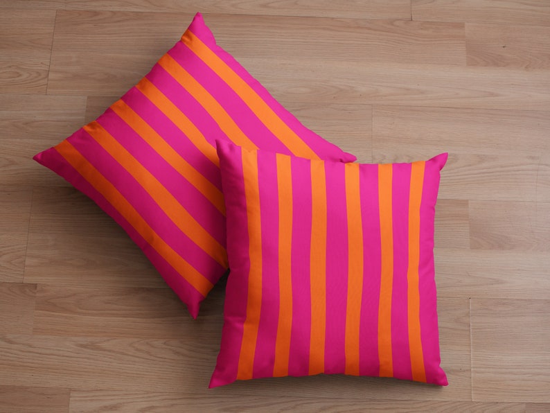 May include: Two decorative throw pillows with a pink and orange striped pattern. The pillows are lying on a wooden floor.