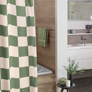 May include: A green and white checkered shower curtain hangs in a bathroom with a white bathtub and a wooden tile wall. A green towel hangs on a towel rack and a small wooden side table with a green towel, a white candle, and a vase with green leaves sits on the floor.