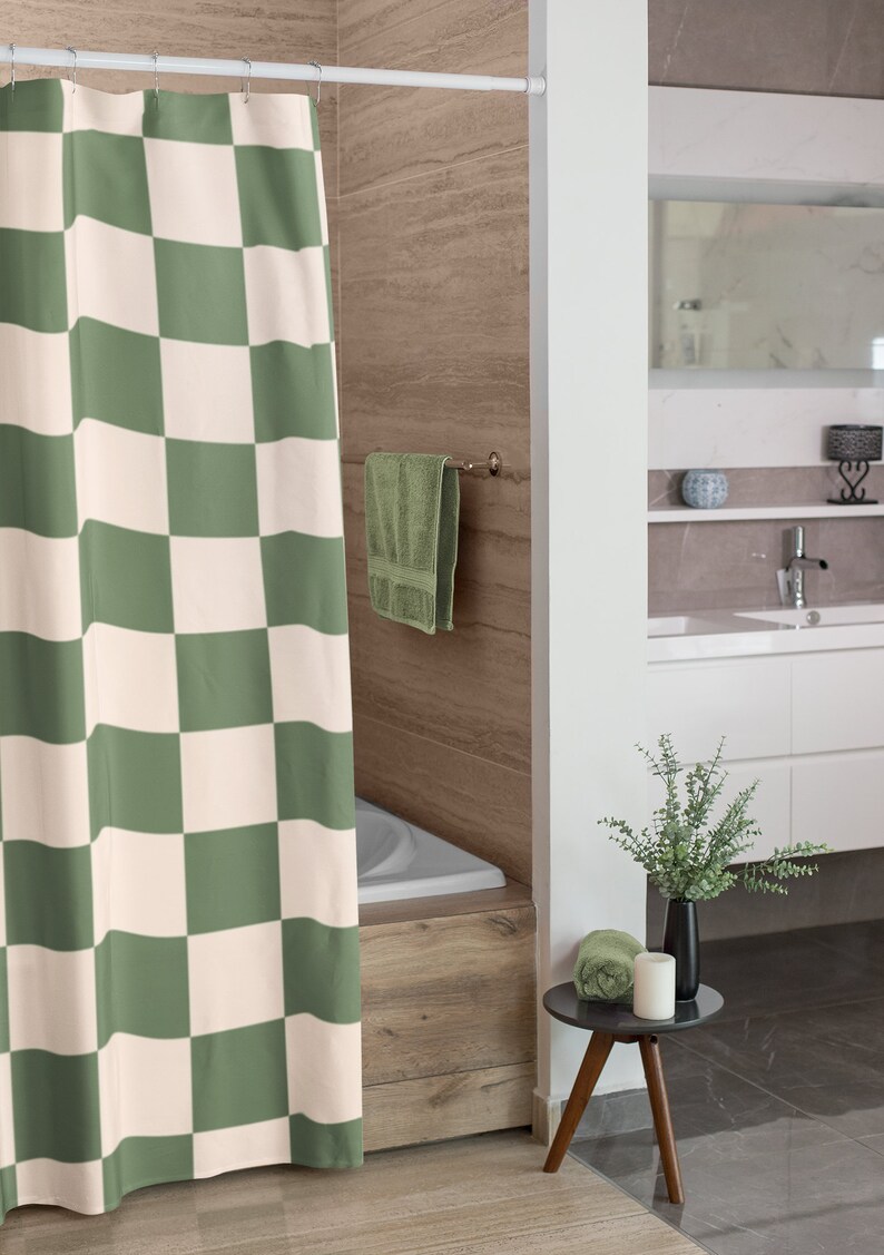 May include: A green and white checkered shower curtain hangs in a bathroom with a white bathtub and a wooden tile wall. A green towel hangs on a towel rack and a small wooden side table with a green towel, a white candle, and a vase with green leaves sits on the floor.