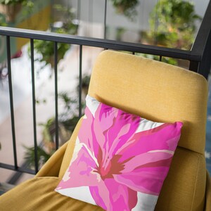 Op de afbeelding: Een gele stoel met een roze bloemenkussen. Het kussen heeft een witte achtergrond en een grote roze bloem met een bruin centrum.