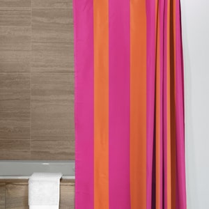 May include: A pink and orange striped shower curtain with white rings hanging from a white shower rod.