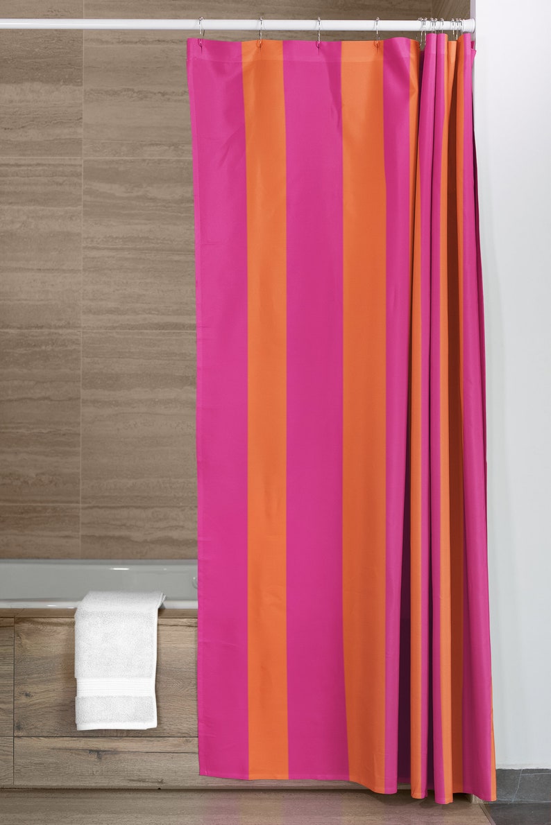 May include: A pink and orange striped shower curtain with white rings hanging from a white shower rod.