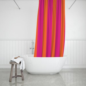May include: A white bathtub with a pink and orange striped shower curtain hanging over the side. The bathtub is in a white bathroom with white tiled walls.