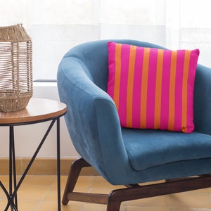 May include: A blue armchair with a pink and orange striped cushion. A woven wicker lantern sits on a wooden side table with a black metal frame.