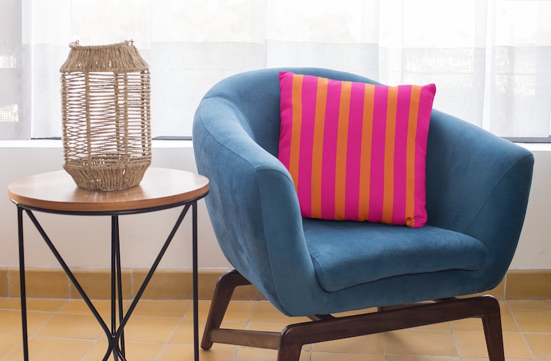 May include: A blue armchair with a pink and orange striped cushion. A woven wicker lantern sits on a wooden side table with a black metal frame.