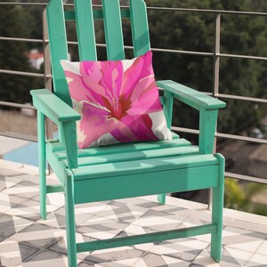 May include: A teal green wooden adirondack chair with a pink floral pillow. The chair is on a black and white tiled patio.