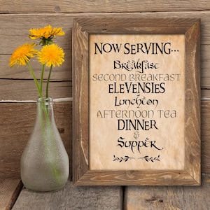 May include: A framed sign with a rustic background and black text that reads "NOW SERVING... Breakfast, Second Breakfast, Elevensies, Luncheon, Afternoon Tea, Dinner & Supper".