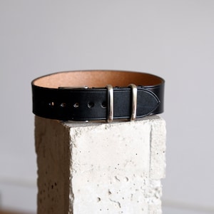 May include: A black leather watch strap with silver buckle and keepers.