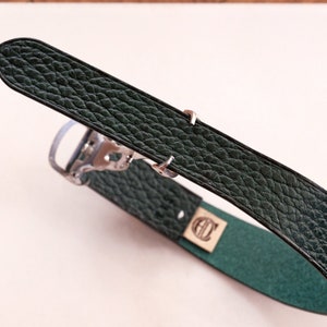 May include: A dark green leather watch strap with a silver buckle. The strap has a textured surface and is folded in half.