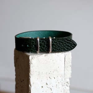 May include: A dark green leather watch strap with silver buckle and keepers.