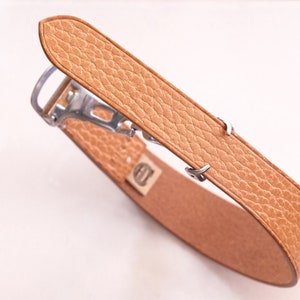 May include: A tan leather watch strap with a silver buckle and a textured surface.