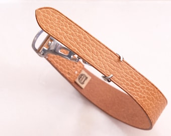 May include: A tan leather watch strap with a silver buckle and a textured surface.