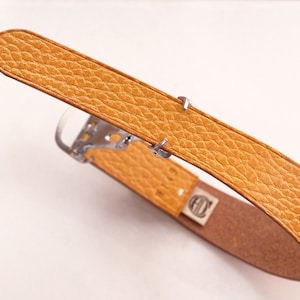 May include: A brown leather belt with a silver buckle. The belt has a textured surface and is folded in half.