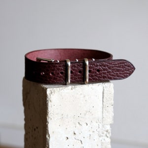 May include: A dark burgundy leather watch strap with silver buckle and three keepers.
