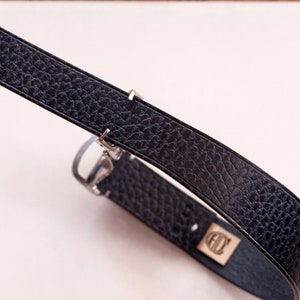 May include: A black leather watch strap with a silver buckle. The strap has a textured surface and is folded in a circle.