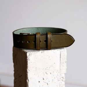 May include: A dark green leather watch strap with a light green lining and a silver buckle.
