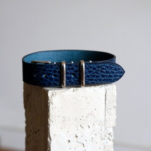 May include: A dark blue leather watch strap with silver buckle and keepers.