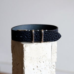 May include: A black leather watch strap with a silver buckle and three silver keepers.