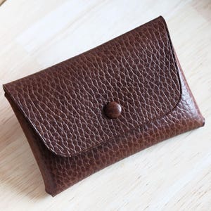 Peut inclure: Un portefeuille en cuir marron foncé avec une surface texturée et une fermeture à bouton. Le portefeuille rectangulaire a un rabat qui se replie pour sécuriser le contenu. Fabriqué en cuir marron foncé.