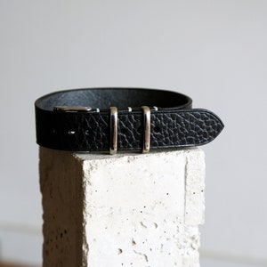 May include: A black leather watch strap with silver buckle and three silver keepers.